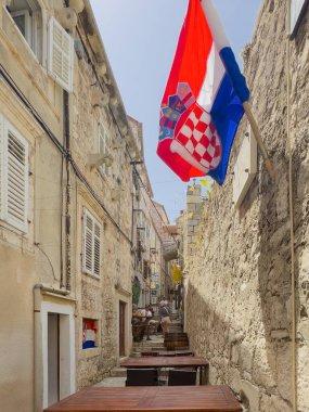 Korcula, Croatia - June 30, 2024: Looking South from ramparts into alley, SV Roka shows flags and tables of Popina Restaurant. People present clipart