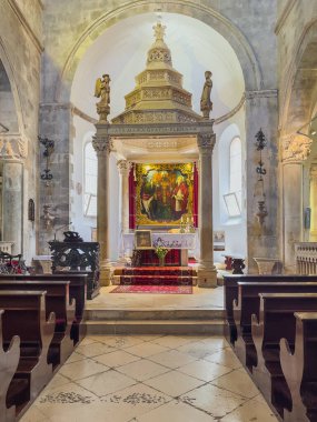 Korcula, Hırvatistan - 30 Haziran 2024: Saint Mark Katedrali. Ana sunak ve sancak, büyük resim ve taş baldaquin ve taş melek heykelleri, önünde siyah ahşap banklar.
