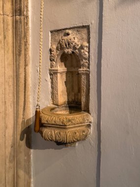 Korcula, Hırvatistan - 30 Haziran 2024: Saint Mark Katedrali. Kapının yanındaki duvarda küçük oyulmuş kutsal su yazı tipi. Çanın kordonu