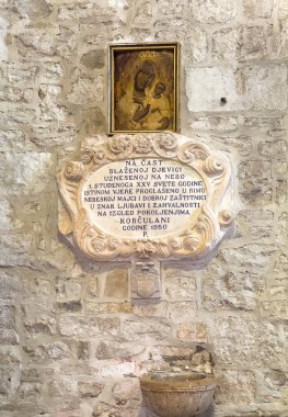 Korcula, Hırvatistan - 30 Haziran 2024: Saint Mark Katedrali. Küçük Meryem Ana tablosu, 1950 'de yapılmış, antik bir duvara karşı yapılmış, altında küçük kutsal su kuyusunun üzerinde oyulmuş bir yazı var.