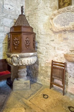 Korcula, Hırvatistan - 30 Haziran 2024: Saint Mark Katedrali. Köşede heykeli üzerinde heykel olan büyük ahşap sekizgen sandıkla kaplı antik yontulmuş taş font.