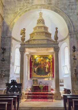 Korcula, Hırvatistan - 30 Haziran 2024: Saint Mark Katedrali. Ana sunak ve sancak, büyük resim ve taş baldaquin ve taş melek heykelleri, önünde siyah ahşap banklar.