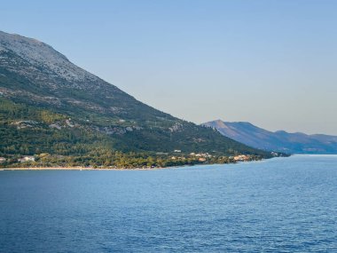 Korcula, Croatia - June 30, 2024: Mainland coastline above Kuciste with tall forested mountain in back. Few buildings along beach