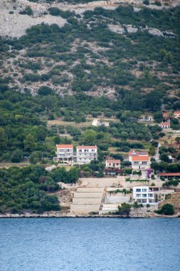 Kuciste, Croatia - June 30, 2024: Mainland coastline of Kuciste with Pension Mirina higher and other residential vacation homes. Mountain slope with some green foliage clipart