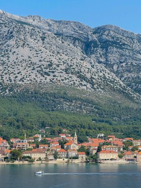 Orebiç, Hırvatistan - 30 Haziran 2024: Adriyatik Denizi kıyısındaki kasaba üzerindeki Orebik kulelerdeki Hristiyanların Mary Kilisesi, hepsi de kırmızı çatılı şehir manzarasında yer alıyor. Arka taraftaki dağ sırası.