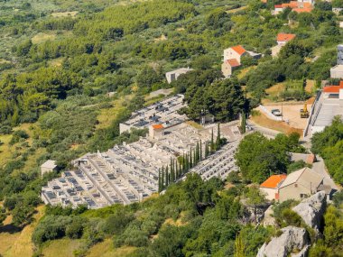 Split, Hırvatistan - 1 Temmuz 2024: Klis Kalesi 'nden sıralanmış mezarlarla birlikte Klis mezarlığı. Çevrede yeşil bitki örtüsü ve kırmızı çatılı evler var.