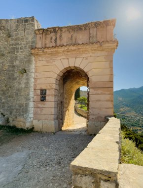 Split, Hırvatistan - 1 Temmuz 2024: Klis Kalesi. Mavi bir gökyüzünün altındaki taş kaldırımın sonundaki kapı gibi metal ızgaralı giriş kapısı. Arkadaki orman dağı.. 