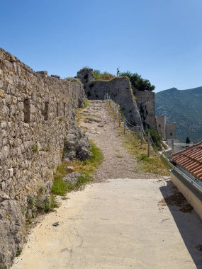 Split, Hırvatistan - 1 Temmuz 2024: Pebbel ve kayalık yol mavi gökyüzünün altındaki Klis Kalesi 'nin üst katına çıkıyor. Çatıdaki kırmızı camlar.