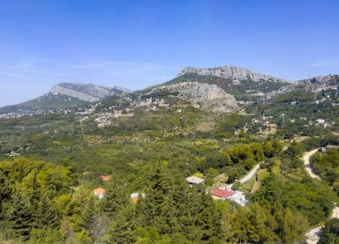 Split, Hırvatistan - 1 Temmuz 2024: Klis Kalesi kalenin altında görünen Kutsal Bakire Meryem Kulesi 'nin Varsayımı Kilisesi ile geniş yeşil manzaralı bir kayanın üzerindedir. Arkasında dağlar, önünde yeşil ağaçlar