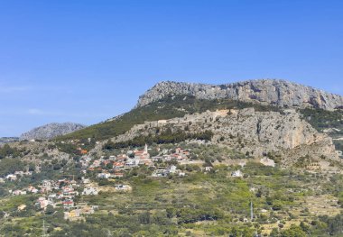 Split, Hırvatistan - 1 Temmuz 2024: Klis Kalesi kalenin altında görünen Kutsal Bakire Meryem Kulesi 'nin Varsayımı Kilisesi ile geniş yeşil manzaralı bir kayanın üzerindedir. Arkasında dağlar, önünde yeşil ağaçlar