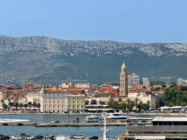 Split, Hırvatistan - 1 Temmuz 2024: Üzerinde Aziz Domnius Katedrali olan tahta kaldırımın arkasındaki tarihi kent. Mavi gökyüzünün altındaki sıradağlarda. Limanın karşısından görüldü. Yeşil kubbeli bir liman binası.