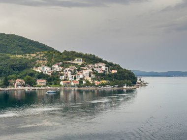 Kotor Körfezi, Karadağ - 2 Temmuz 2024: Kamenari köyünün güney manzaralı Lepetane-Kamenari feribotu yanaştı. Kasaba ormanlık dağa karşı kıyı şeridine kurulmuş. Kırmızı çatılı beyaz evlerin şehir manzarası