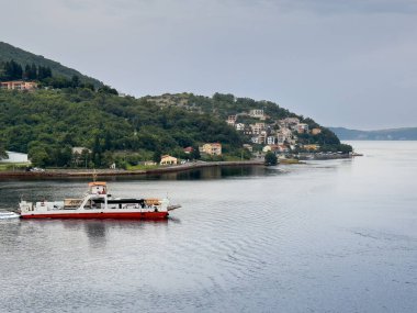 Kotor Körfezi, Karadağ - 2 Temmuz 2024: Igalo Ferry Lepetane terminalinden ayrıldı. Kuzeyden yeşil dağın yamacına kurulmuş kasabanın manzarası