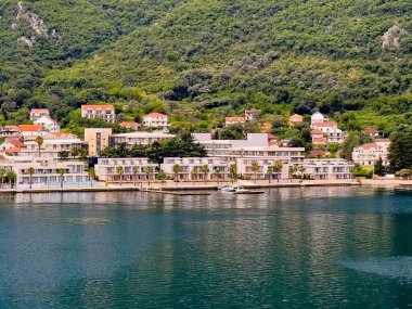 Bay of Kotor, Montenegro - July 2, 2024: Hyatt Regency Hotel, North facade closeup, at Donji Stoliv built on peninsula coastline in cityscape of red-roofed buildings. Beach and boats clipart