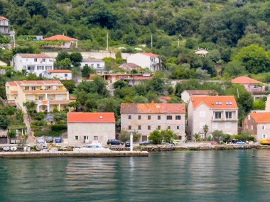 Kotor Körfezi, Karadağ - 2 Temmuz 2024: Muo köyü. Kıyı şeridi, birkaç yat ve botla küçük bir limana yakın. Kırmızı çatılı evler ve yeşil ağaçlı apartmanlar.