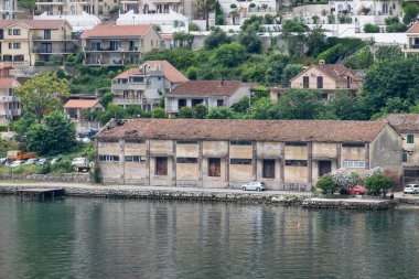 Kotor Körfezi, Karadağ - 2 Temmuz 2024: Muo köyü. Kıyı şeridi, rıhtımdaki tarihi depo. Daire ve apartman binaları.