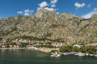 Kotor, Karadağ - 2 Temmuz 2024: Manzara. Yat limanının yakınındaki rıhtımda özgürlüğün Obelisk 'i, kasabanın arkasındaki şehir manzarası, parkın yeşil ağaçları. Mavi bulutların altındaki dağ sırası