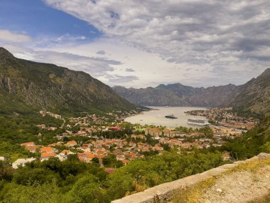 Kotor, Karadağ - 2 Temmuz 2024: Kotor kenti körfezinde gri bulutlar altında P22 dağ yolundan görüldü. Her yerde dağlar ve limanda gemiler