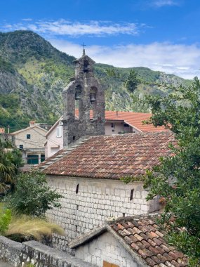 Kotor, Karadağ - 2 Temmuz 2024: Skaljari Mahallesi 'nde çan kulesi olan küçük Saint Dujam Kilisesi. Dağlar mavi bulutların altında