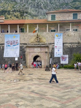 Kotor, Karadağ - 2 Temmuz 2024: Eski tarihi kentin surlarından ana giriş. Etrafta bir sürü insan dolaşıyor. Duvarda büyük pankartlar, arkada dağ