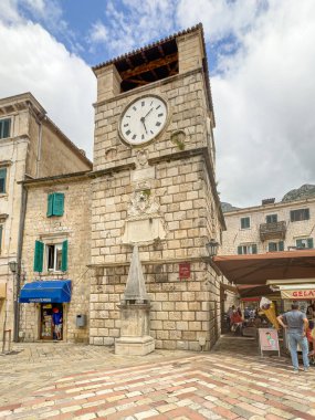 Kotor, Karadağ - 2 Temmuz 2024: Ana girişi geçince, mavi bulutların altındaki tarihi kentte saat kulesi. Mevcut insanlar