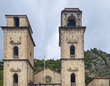 Kotor, Karadağ - 2 Temmuz 2024: Eski tarihi şehir merkezi. Aziz Tryphon Katedral kuleleri mavi bulutlara ve dağ kayalarına karşı