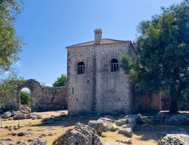 Meospotamos, Yunanistan - 3 Temmuz 2024: Acheron Necromanteion. Mavi gökyüzünün altındaki tek bir binanın batı cephesi. Bahçede yeşil yapraklar ve kayalar