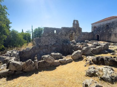 Meospotamos, Greece - July 3, 2024: Necromanteion of Acheron. Deep trench, ex cave in garden under blue sky. Building and Christian chapel ruin in back clipart