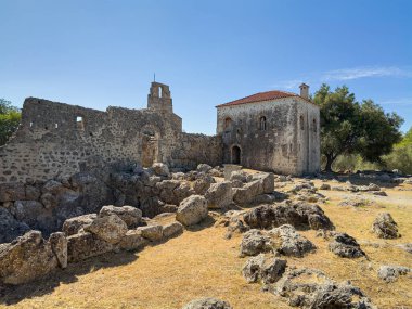 Meospotamos, Yunanistan - 3 Temmuz 2024: Acheron Necromanteion. Mavi gökyüzünün altında kırmızı çatılı ve arkasında yeşil yapraklı bir binanın kuzey cephesi. Bahçedeki kayaların çizgileri