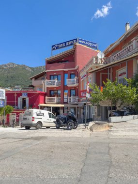 Parga, Yunanistan - 3 Temmuz 2024: Araç kiralama, sigorta şirketlerinden, mavi gökyüzü altında yeşil ormanlı dağlara kadar farklı iş stillerine sahip küçük alışveriş merkezleri.