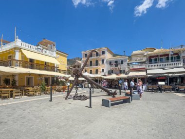 Parga, Yunanistan - 3 Temmuz 2024: Mavi gökyüzünün altında Horeca binaları bulunan liman rıhtımının önündeki dev çapa