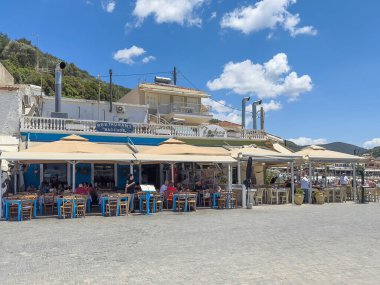 Parga, Yunanistan - 3 Temmuz 2024: Boardwalk 'taki Restoran Bacchos. Mavi bulutların altında insanlar var. Masalar ve sandalyeler