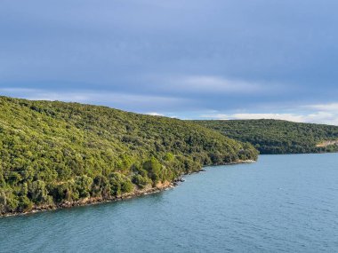 Igoumenitsa, Yunanistan - 3 Temmuz 2024: Liman. Güney kıyısı boyunca mavi gökyüzünün altındaki limanın dışında elektrik hatları var. Yol yok.