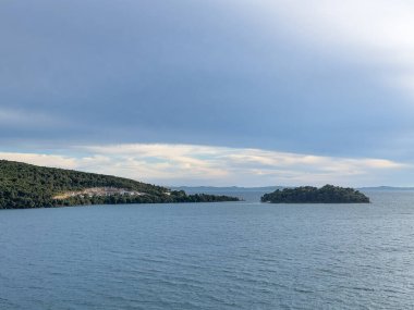 Igoumenitsa, Yunanistan - 3 Temmuz 2024: Anakara yarımadası ve tapınağındaki taş ocağı, Yaşam Veren Baharın küçük yeşil ormanlık kutsal adasında, mavi bulutların altında