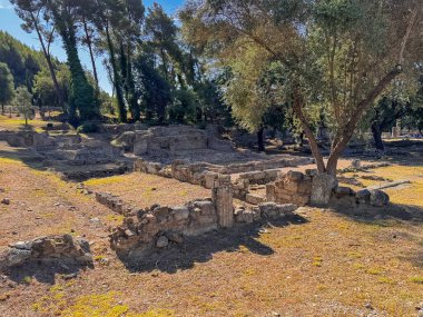 Olympia, Yunanistan - 4 Temmuz 2024: Olimpiyat Oyunlarının doğduğu yer. Eski esaslar, ağaçların altında solda, Kronion Thermae