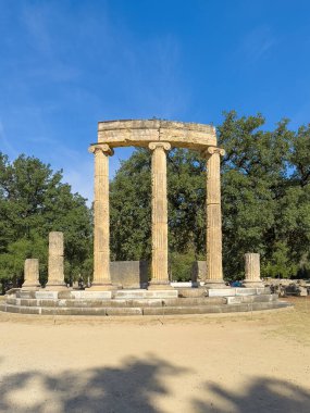 Olympia, Yunanistan - 4 Temmuz 2024: Olimpiyat Oyunlarının doğduğu yer. Mavi gökyüzünün altındaki yeşil ağaçla desteklenen Filipinli harabe