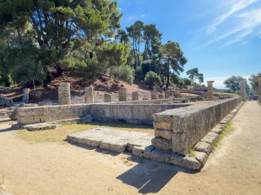 Olympia, Yunanistan - 4 Temmuz 2024: Olimpiyat Oyunlarının doğduğu yer. Hera Tapınağı 'nın dikdörtgen tabanı mavi gökyüzünün altındaki tepede yeşil ağaçlarla desteklenir.
