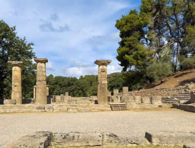 Olympia, Yunanistan - 4 Temmuz 2024: Olimpiyat Oyunlarının doğduğu yer. Hera Tapınağı 'nın doğu tarafındaki sütunlarda mavi bulutların altında yeşil ağaç yaprakları var.