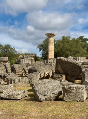 Olympia, Yunanistan - 4 Temmuz 2024: Olimpiyat Oyunlarının doğduğu yer. Zeus Tapınağı 'nın önündeki sütun parçalarının arasında yeşil yapraklar ve kalın mavi bulutlar görülebilir.