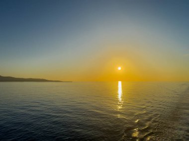 İyon Denizi, Sicilya 'nın doğusu, İtalya - 5 Temmuz 2024: Gündoğumu rengi gökyüzü ve deniz mavisi, ufukta sarı parıltı. Kıyı şeridi görünür