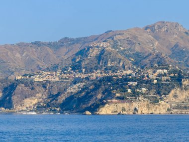 Taormina, Sicilya, İtalya - 5 Temmuz 2024: Taormina sehri deniz seviyesinden yüksektir. Yat limanı, üzerinde büyük UNAHOTELS Capotaormina ile Isola Balle uçurumları tarafından korunuyor. Dağ sıraları, mavi gökyüzü ve deniz