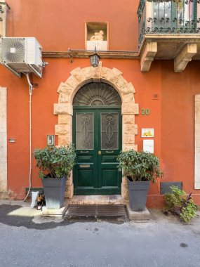 Taormina, Sicilya, İtalya - 5 Temmuz 2024: Casa Lioness, üzerinde hayvan heykeli olan giriş kapısını yonttu. Kırmızı cephe, yeşil kapı ve bej rengi taş çerçeve. Öndeki çömleklerde yeşil bitkiler. Büyük AC 