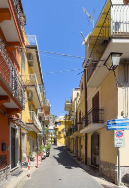 Taormina, Sicilya, İtalya - 5 Temmuz 2024: Daire binaları olan Degli Strategi yolu, dört katlı, mavi gökyüzünün iki tarafında. Çoğunlukla sarı ya da bej cepheler