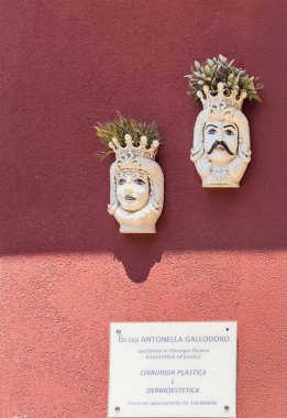 Taormina, Sicilya, İtalya - 5 Temmuz 2024: Kadın yüzü olarak yontulmuş iki beyaz seramik saksı ya da Doktor Ofisi 'nin duvarında asılı duran bir erkek. Plastik Cerrah Antonella Gallodoro.