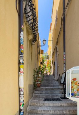 Taormina, Sicilya, İtalya - 5 Temmuz 2024: Alita Francesco de Luna dar yolu Corso Umberto 'daki sarı cephelerin arasındaki merdivenlerden yukarı çıkıyor.