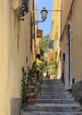 Taormina, Sicilya, İtalya - 5 Temmuz 2024: Alita Francesco de Luna dar sokağı Corso Umberto 'daki sarı cephelerin arasında merdivenlerden yukarı çıkıyor.