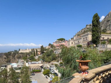 Taormina, Sicilya, İtalya - 5 Temmuz 2024: Mavi gökyüzü altında Roma yoluyla şehir merkezindeki Halk Bahçesi 'nin batısında bulunan saraylar. Arkadaki dağ, bir sürü yeşil yaprak.