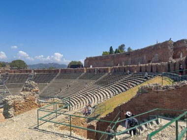 Taormina, Sicilya, İtalya - 5 Temmuz 2024: Antik Yunan tiyatrosunda ya da Teatro antico 'da mavi bulutlar altında oturma alanının SW tarafı. Koruyucu dış duvarın kalıntıları