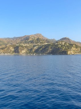 Taormina, Sicilya, İtalya - 5 Temmuz 2024: denizden Taormina 'ya yaklaşıyoruz. Kasaba, arkasında daha yüksek dağlar olan bir plato üzerine inşa edilmiştir. İyon Denizi 'ndeki yatlar mavi su