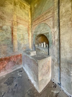 Pompeii, Campania, İtalya - 6 Temmuz 2024: Antik Roma şehri kalıntıları. Casa del Menandro. Köşede küçük bir atadan kalma sunak. Eski boyalı duvarların renkleri kaldı